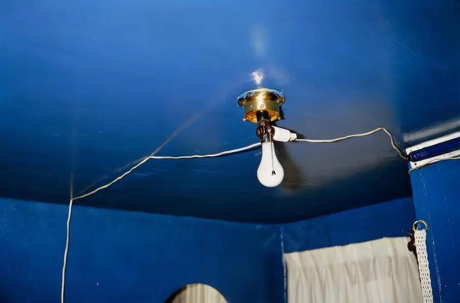 Colour photograph of a blue ceiling with a naked lightbulb fixture hanging from the ceiling.